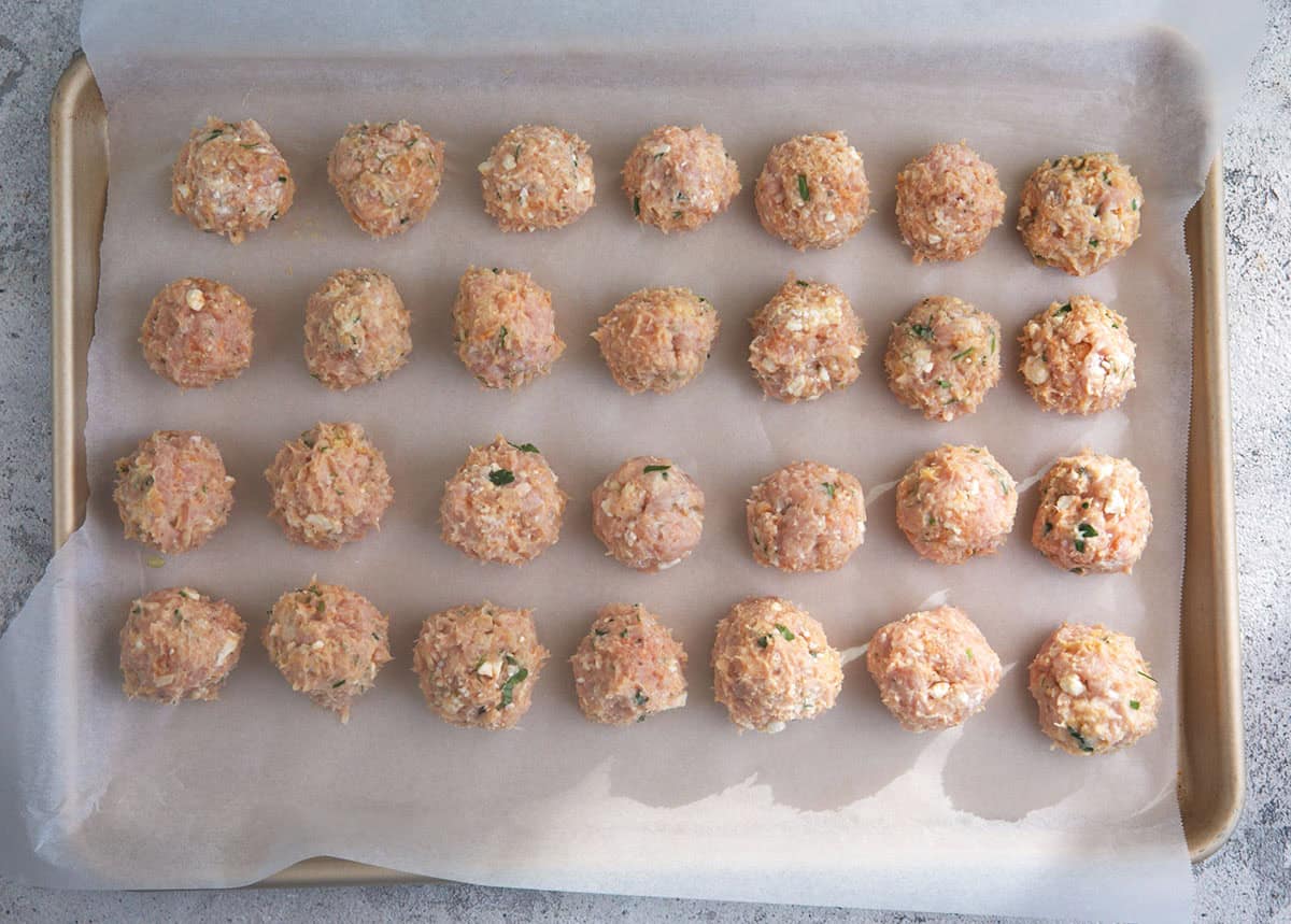 Greek chicken meatballs on a baking sheet ready to be baked