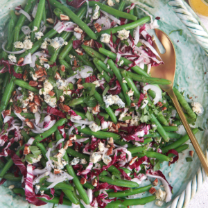 Green bean salad on a green platter with a gold serving spoon.