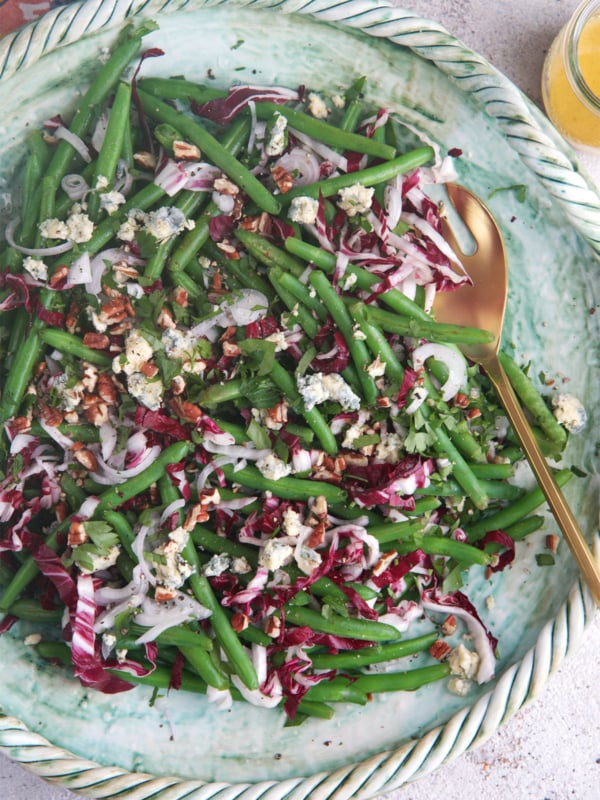 Green bean salad on a green platter with a gold serving spoon.