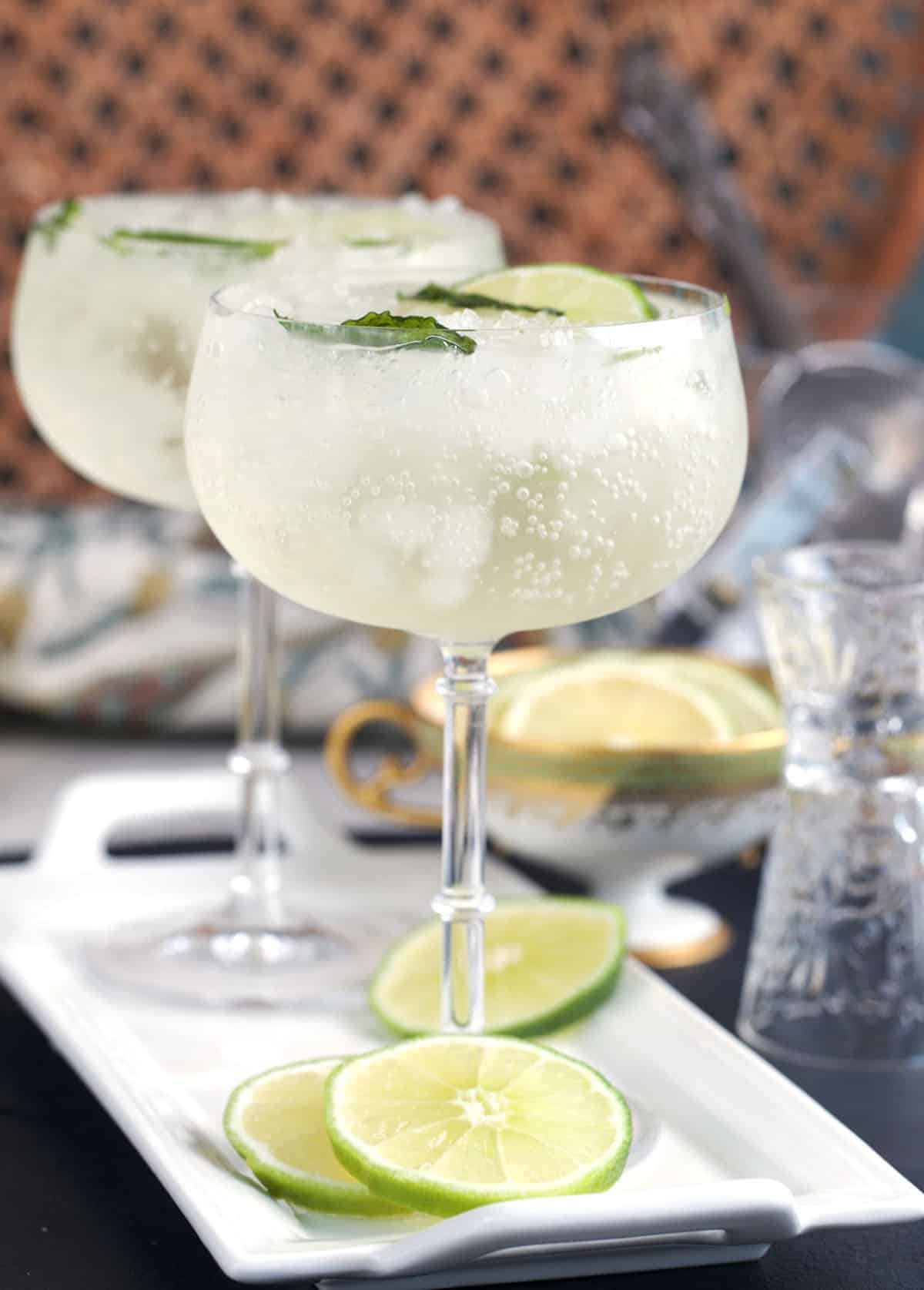 Two glasses with Hugo spritz on a white tray with lime slices