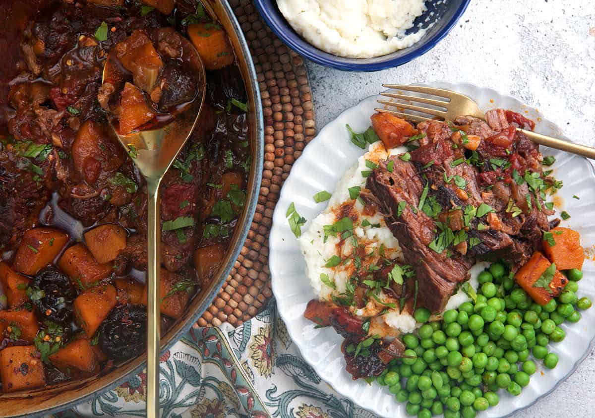 The best pot roast recipe in a dutch oven with a plate topped with sliced roast with peas