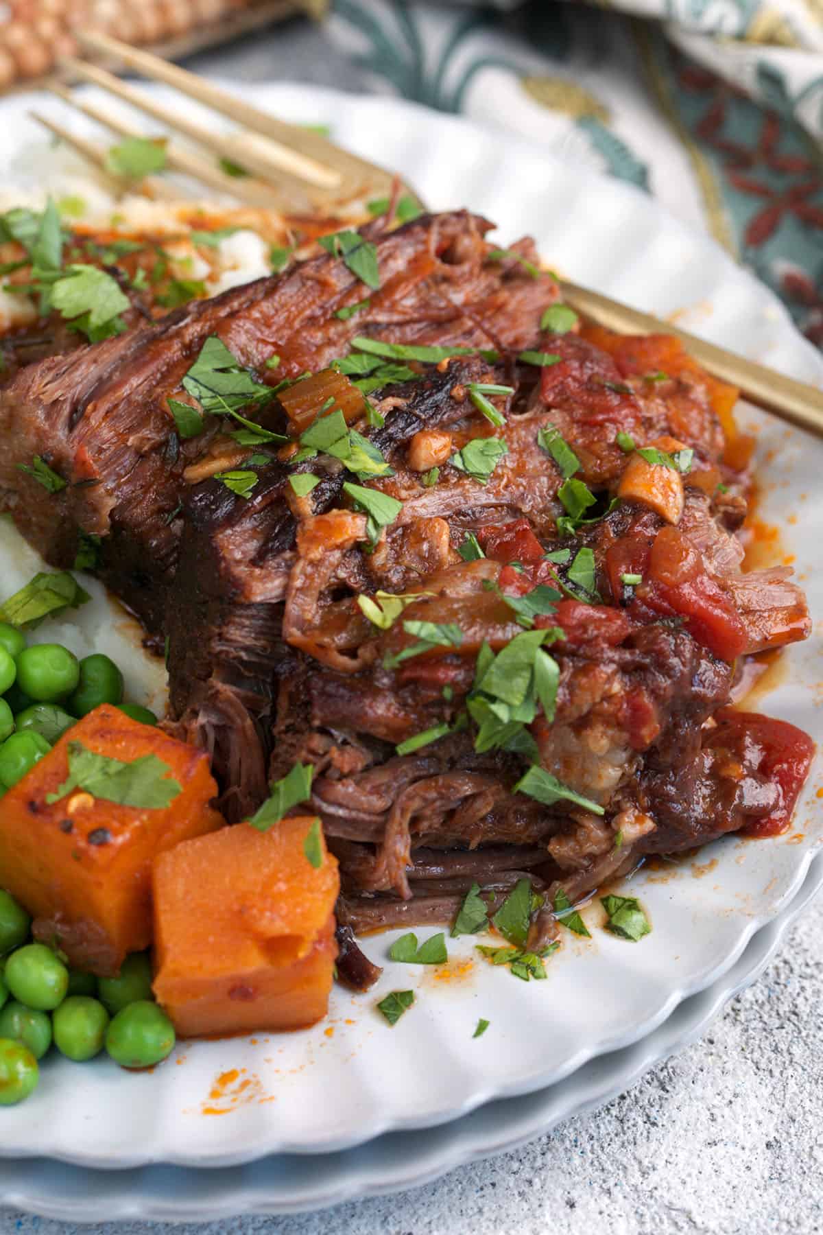 Sliced braised chuck roast on a plate with peas and butternut squash