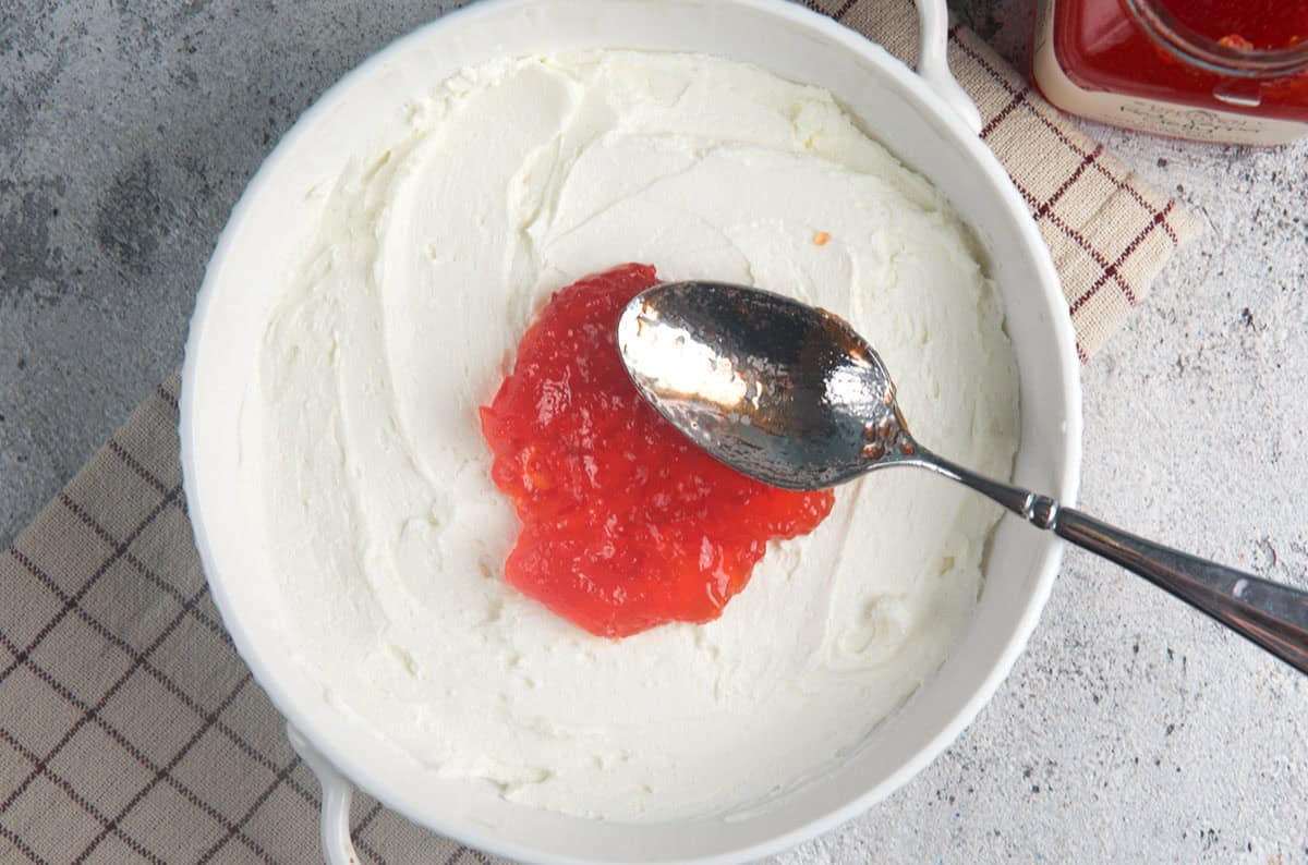 Cream Cheese Dip in a white dish with pepper jelly being spread on top.