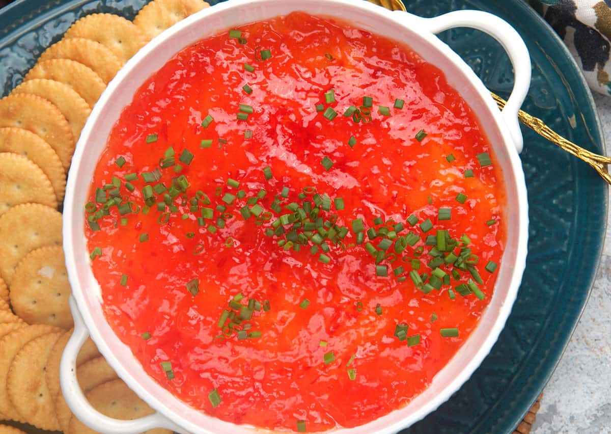 Pepper Jelly Cream Cheese appetizer dip in a white dish with crackers on the side.
