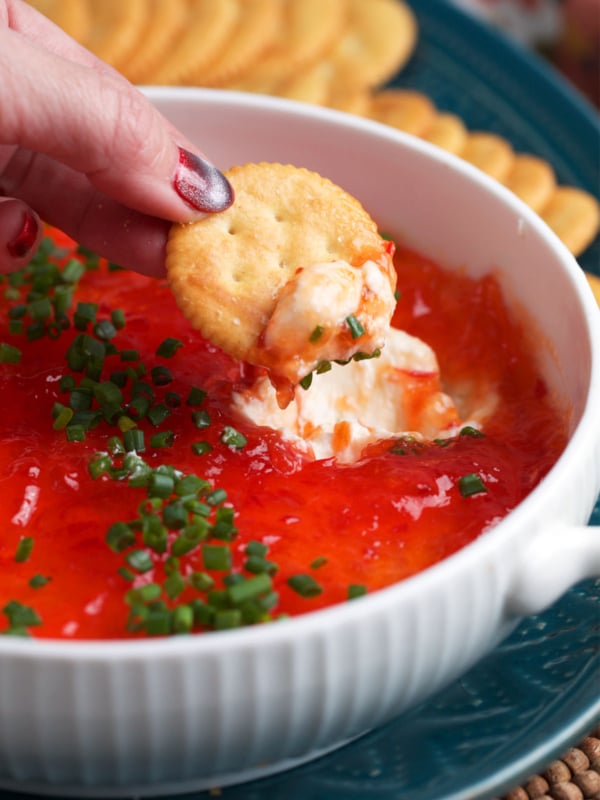 Pepper Jelly Cream Cheese Dip in a white dish with a cracker scooping up some dip