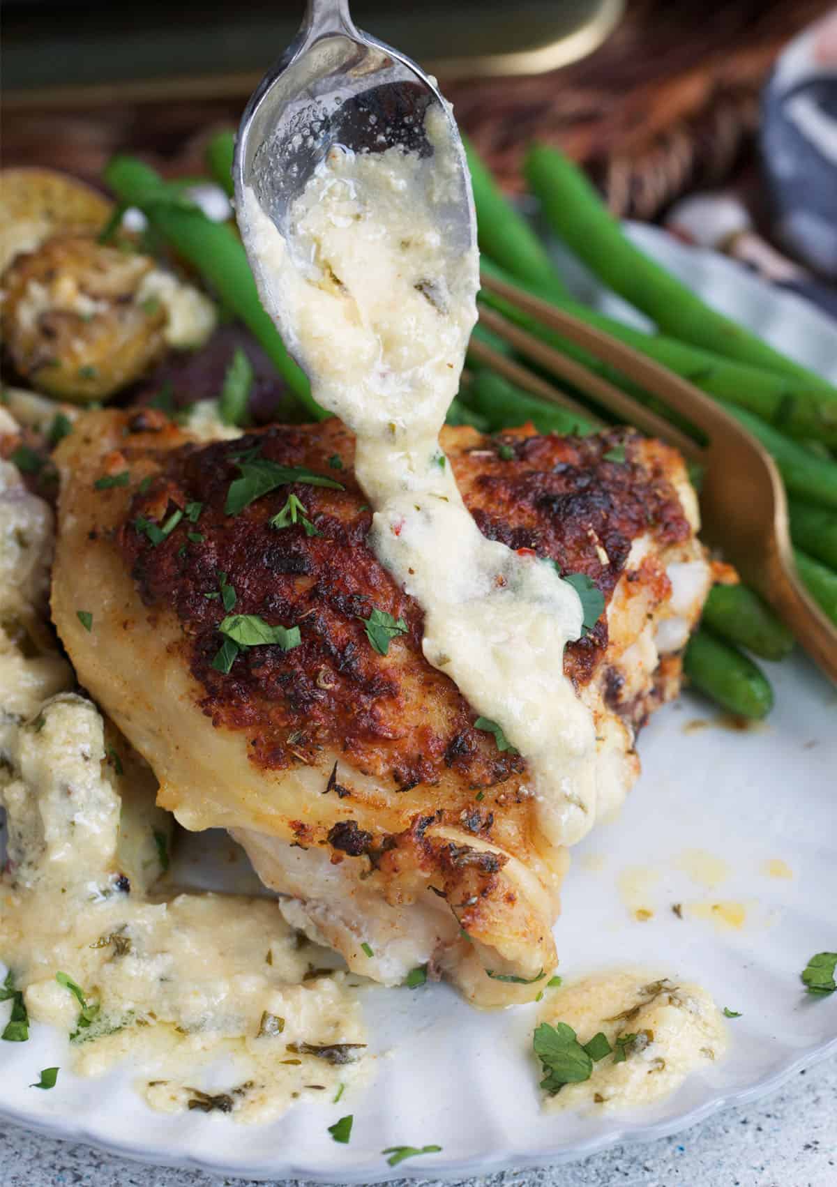 chicken thigh with garlic parmesan sauce being spooned over top.