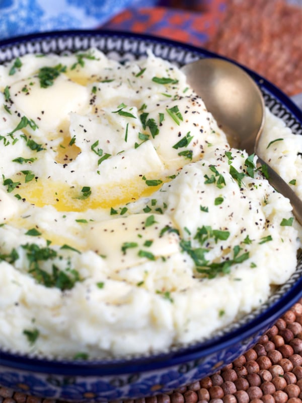Boursin cheese mashed potatoes in a serving bowl and topped with melted butter.