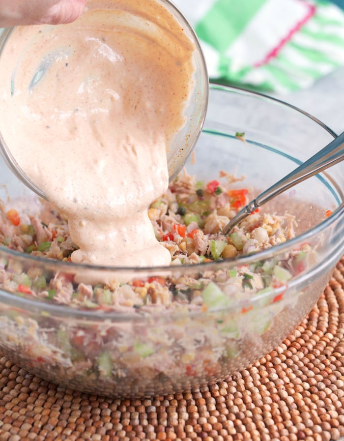 dressing being poured over chickpea tuna salad in a glass mixing bowl