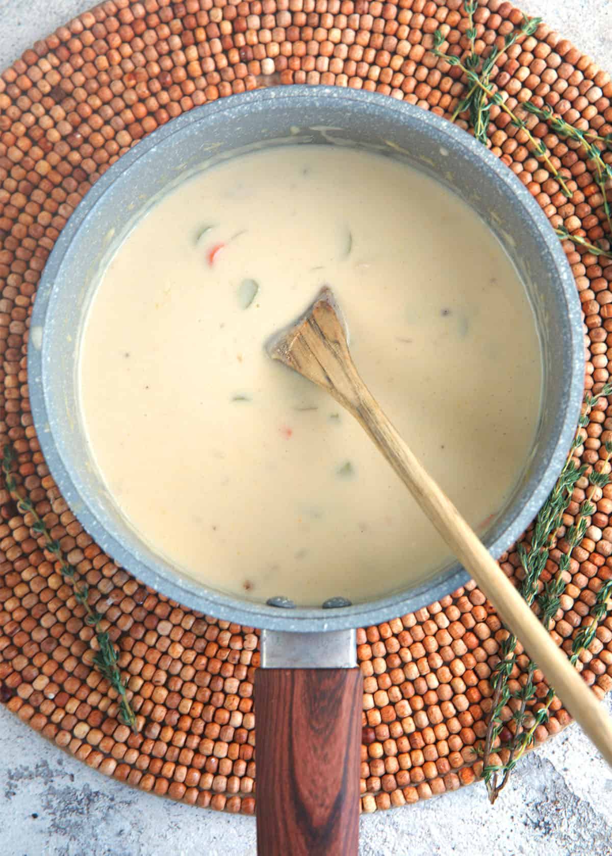 From Scratch Cream of chicken soup simmering in a saucepan with a wooden spoon.