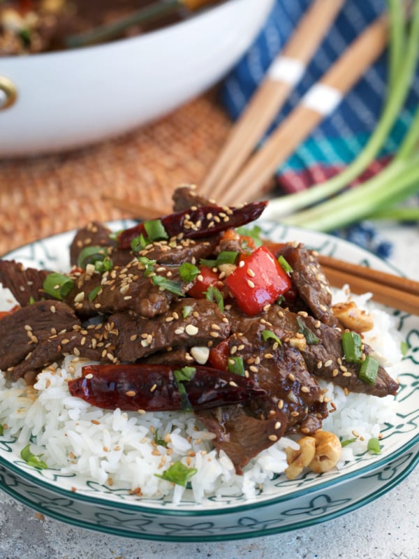 Kung Pao Beef stir fry on rice with chopsticks plated for serving.