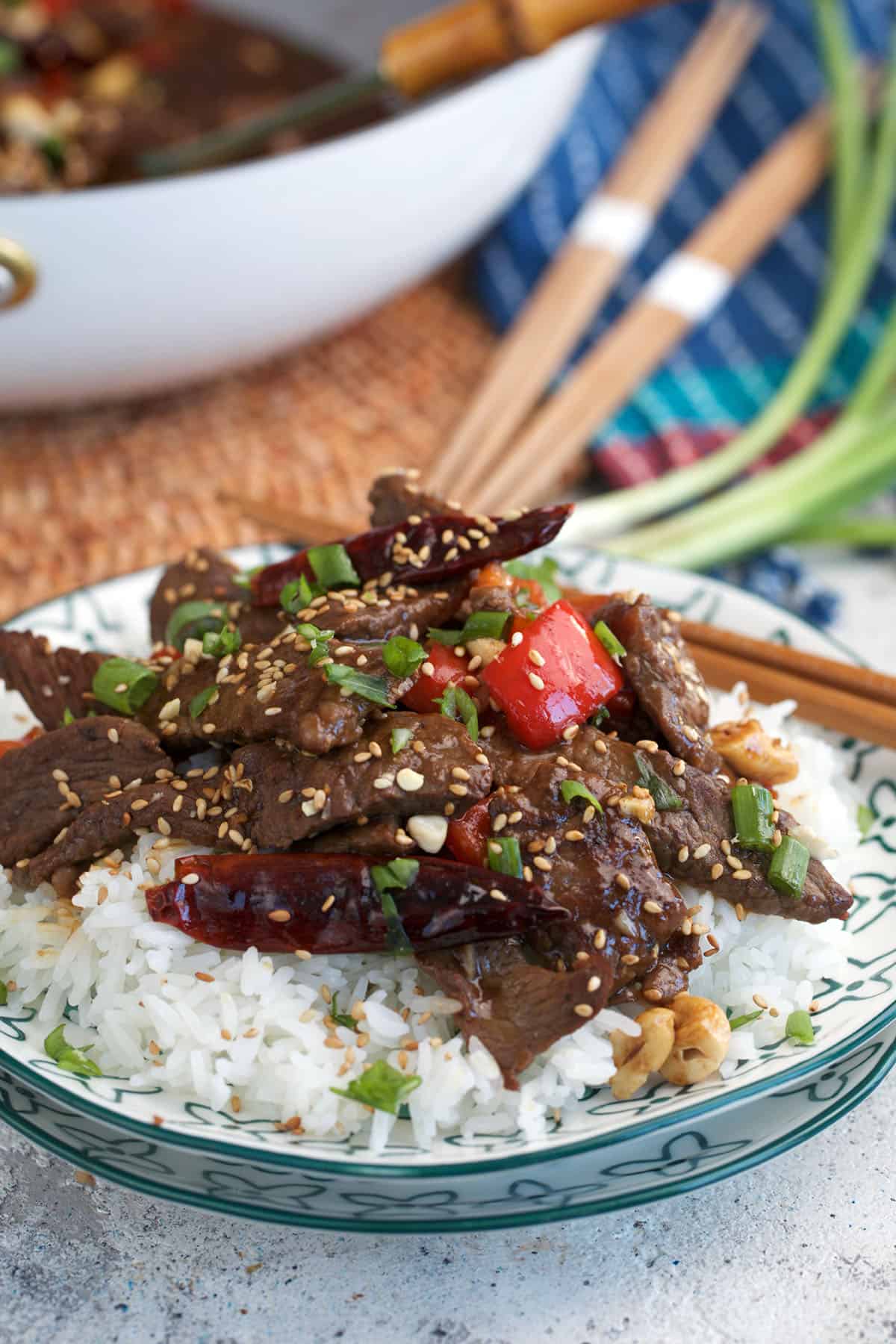 Kung Pao Beef stir fry on rice with chopsticks plated for serving.