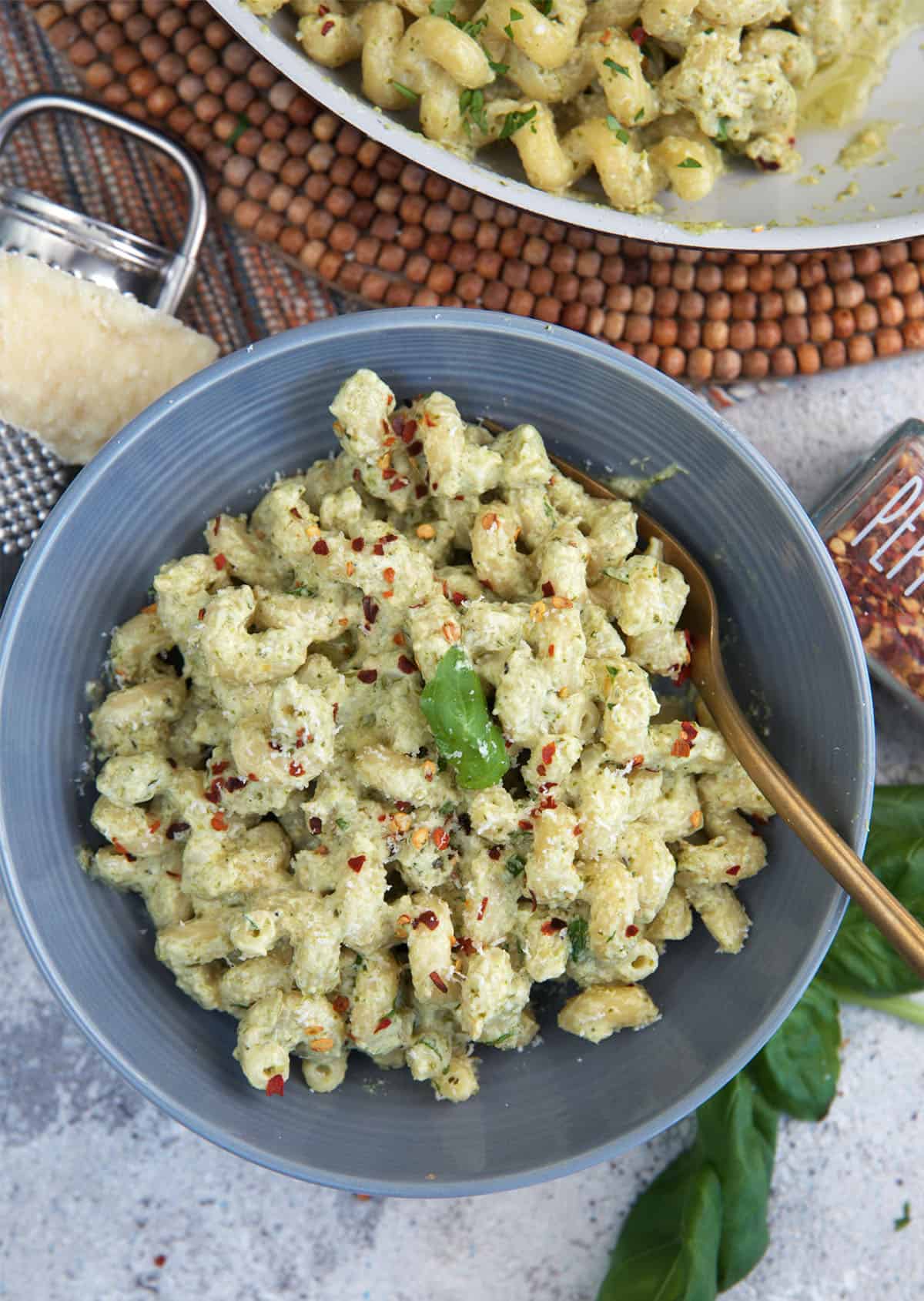 pesto cream sauce with pasta in a gray bowl with a gold fork