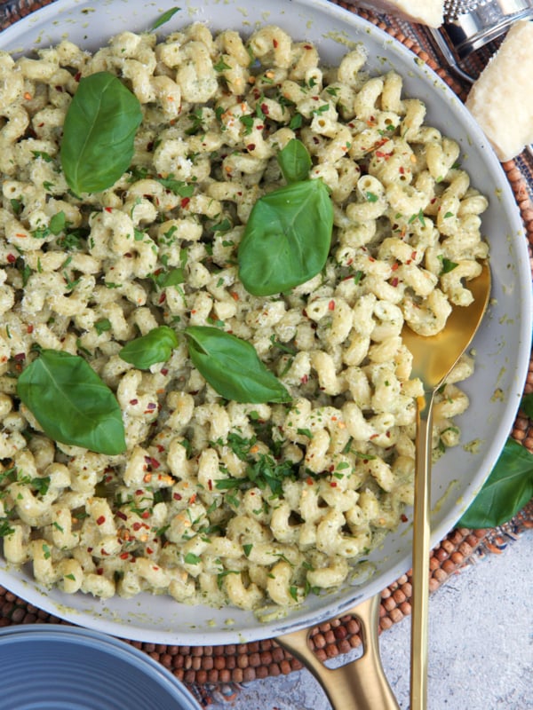 Pesto Cream Sauce tossed with pasta in a skillet and topped with fresh basil leaves for garnish.
