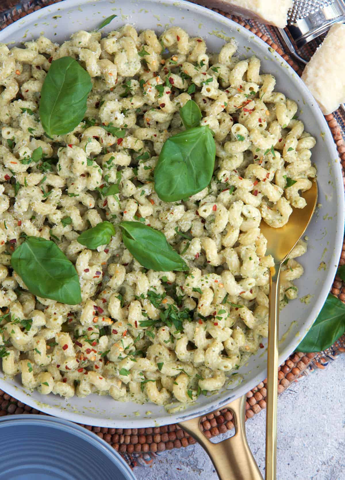 Pesto Cream Sauce tossed with pasta in a skillet and topped with fresh basil leaves for garnish.