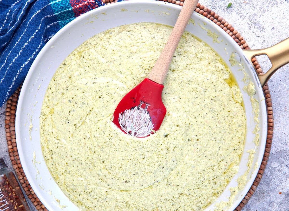 Pesto cream sauce in a skillet with a spatula.