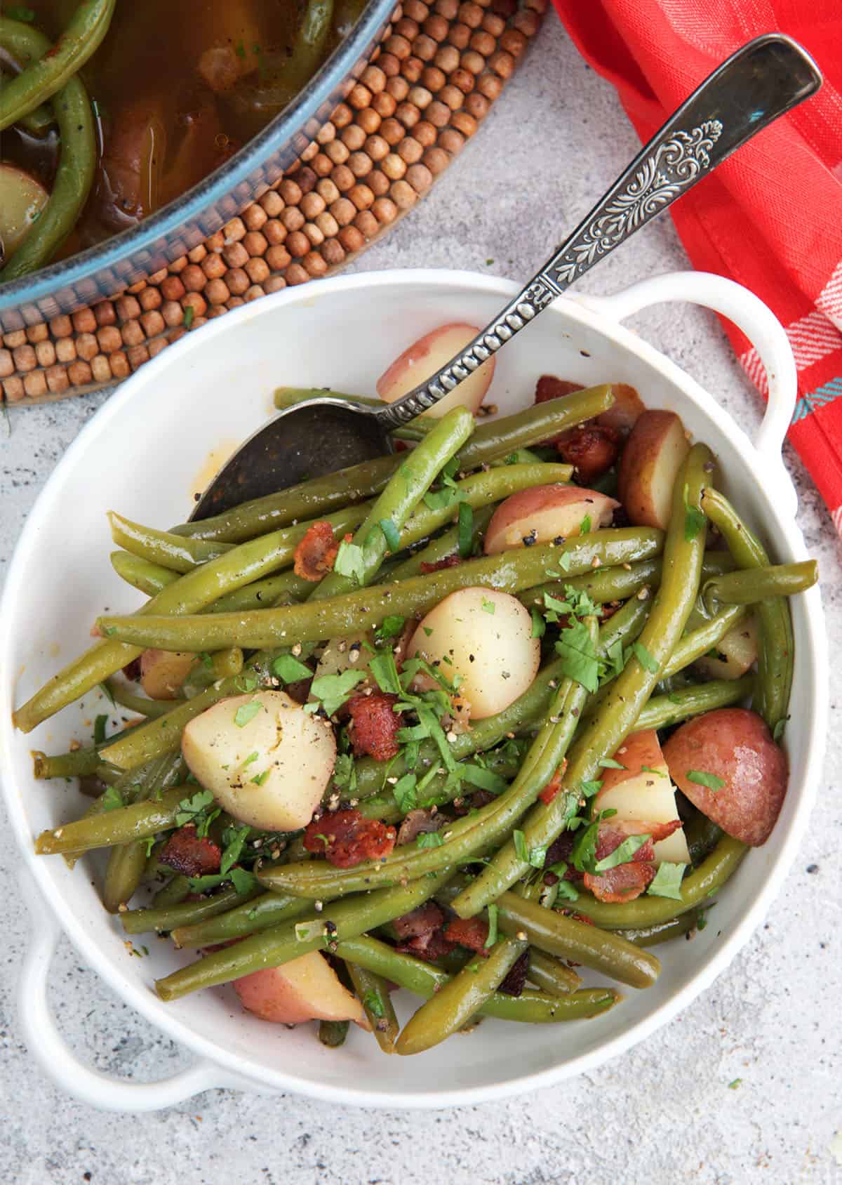 Southern green beans in a white serving dish with a spoon ready to be served.