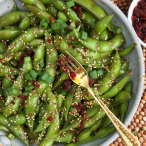 Spicy Edamame appetizer in a white bowl with dipping sauce.