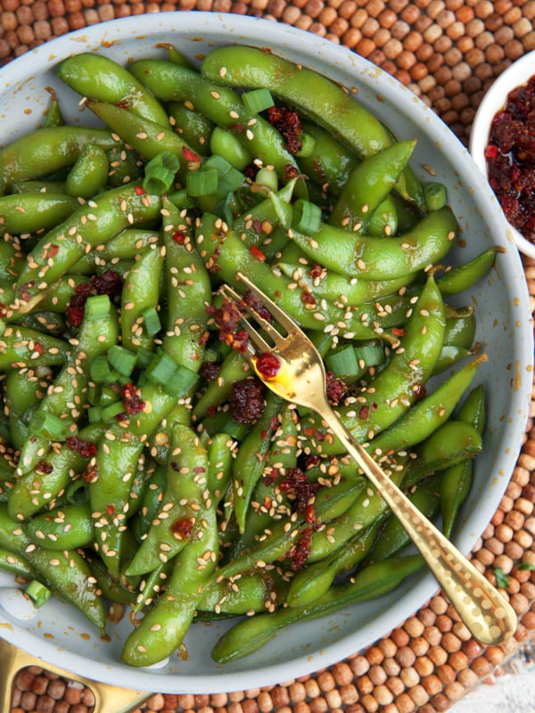 Spicy Edamame appetizer in a white bowl with dipping sauce.