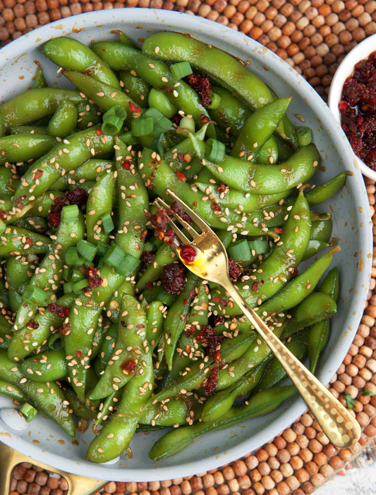 Spicy Edamame appetizer in a white bowl with dipping sauce.