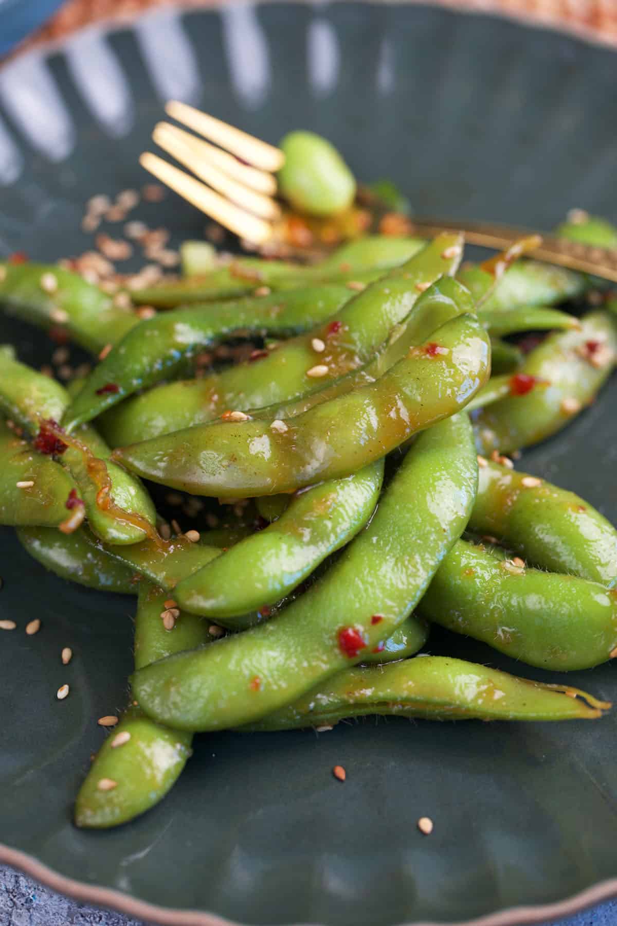 chili crisp edamame on a plate with a gold fork.