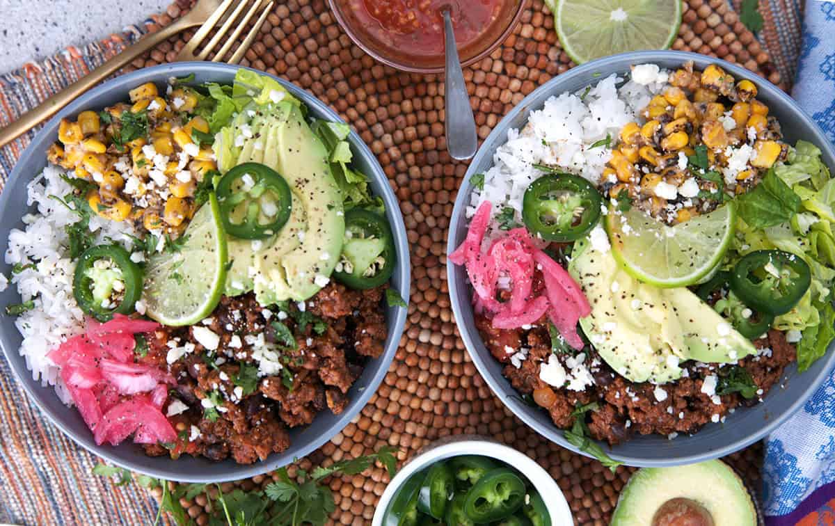 Ground beef taco bowls on a placemat with bowls of toppings around to create a one of a kind taco bowl.