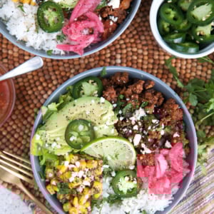 Taco Bowl recipes with ground beef on top of a bowl of rice and toppings of jalapeño, avocado, Mexican street corn and pickled red onions.