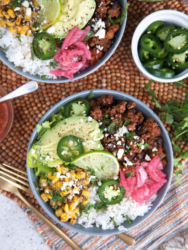 Taco Bowl recipes with ground beef on top of a bowl of rice and toppings of jalapeño, avocado, Mexican street corn and pickled red onions.