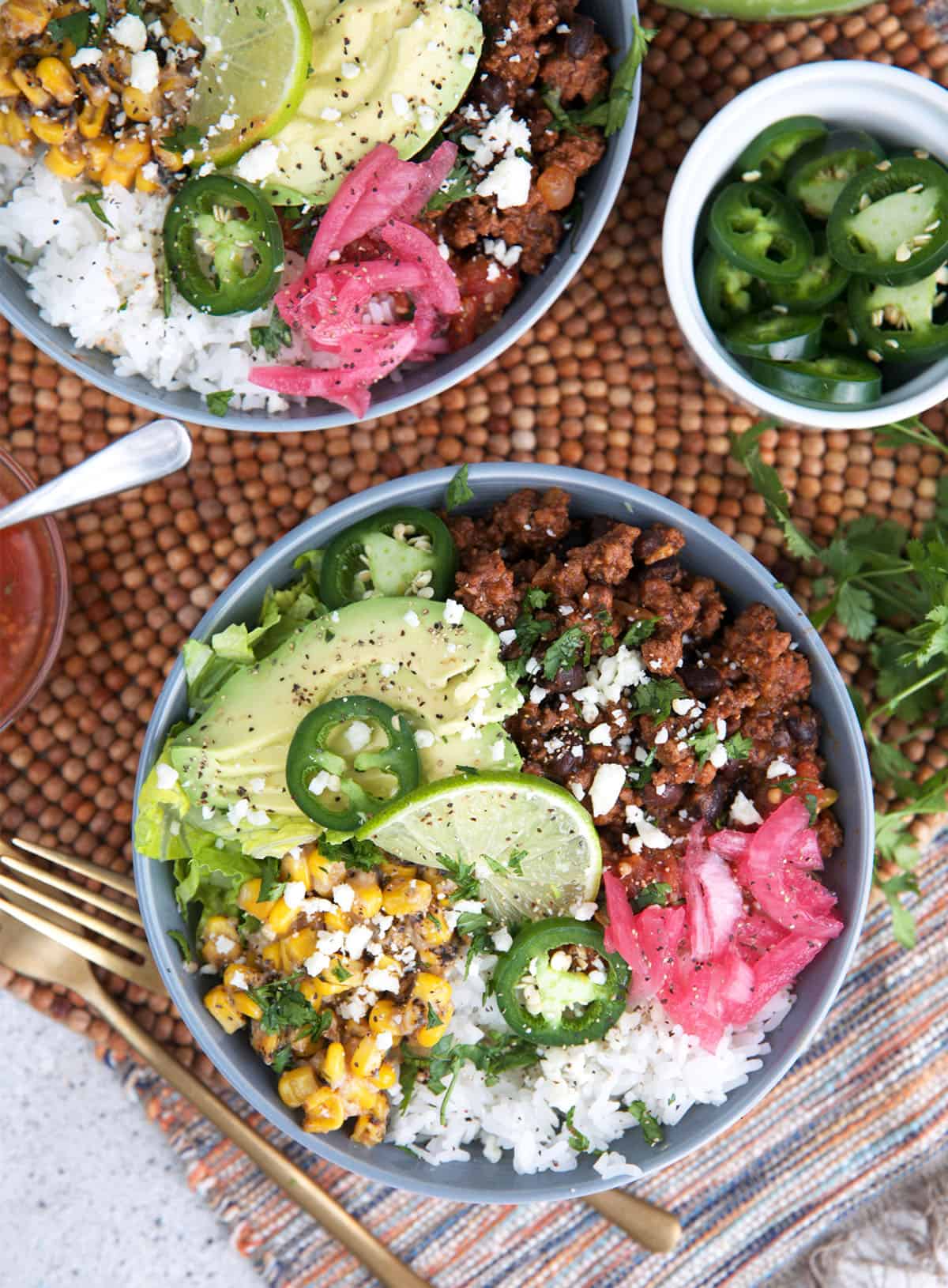 Taco Bowl recipes with ground beef on top of a bowl of rice and toppings of jalapeño, avocado, Mexican street corn and pickled red onions.