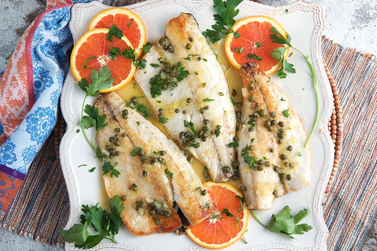 Branzino filets on a platter with orange slices.