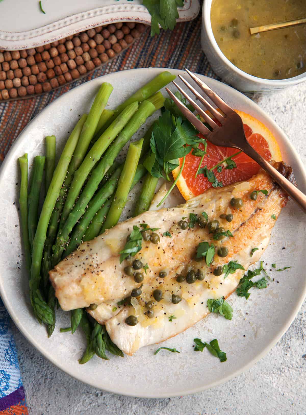 Bronzino fish plated with asparagus and a slice of orange.