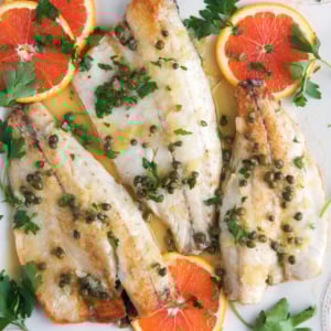 Pan Seared Bronzino filets on a white platter with sliced oranges and parsley