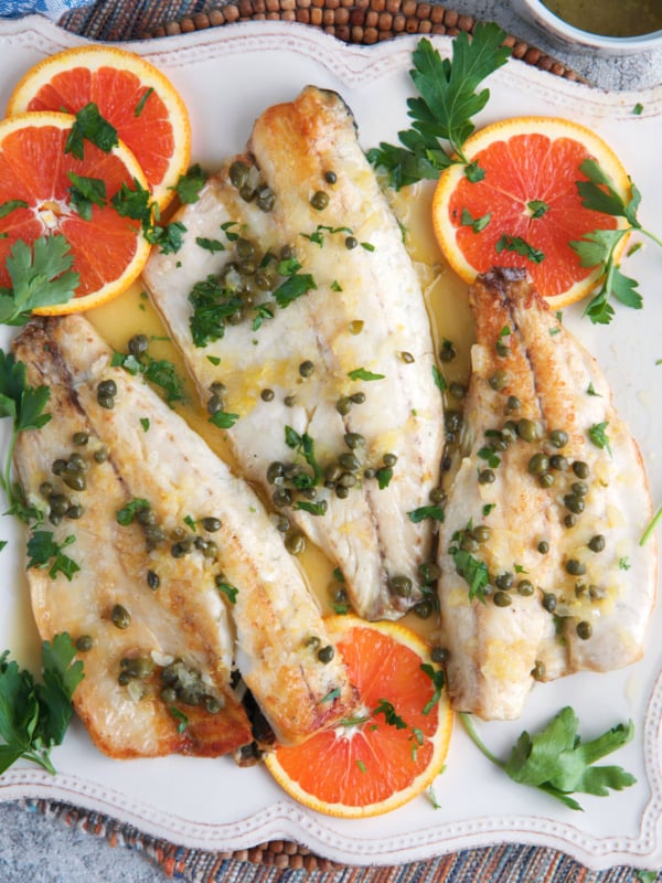 Pan Seared Bronzino filets on a white platter with sliced oranges and parsley