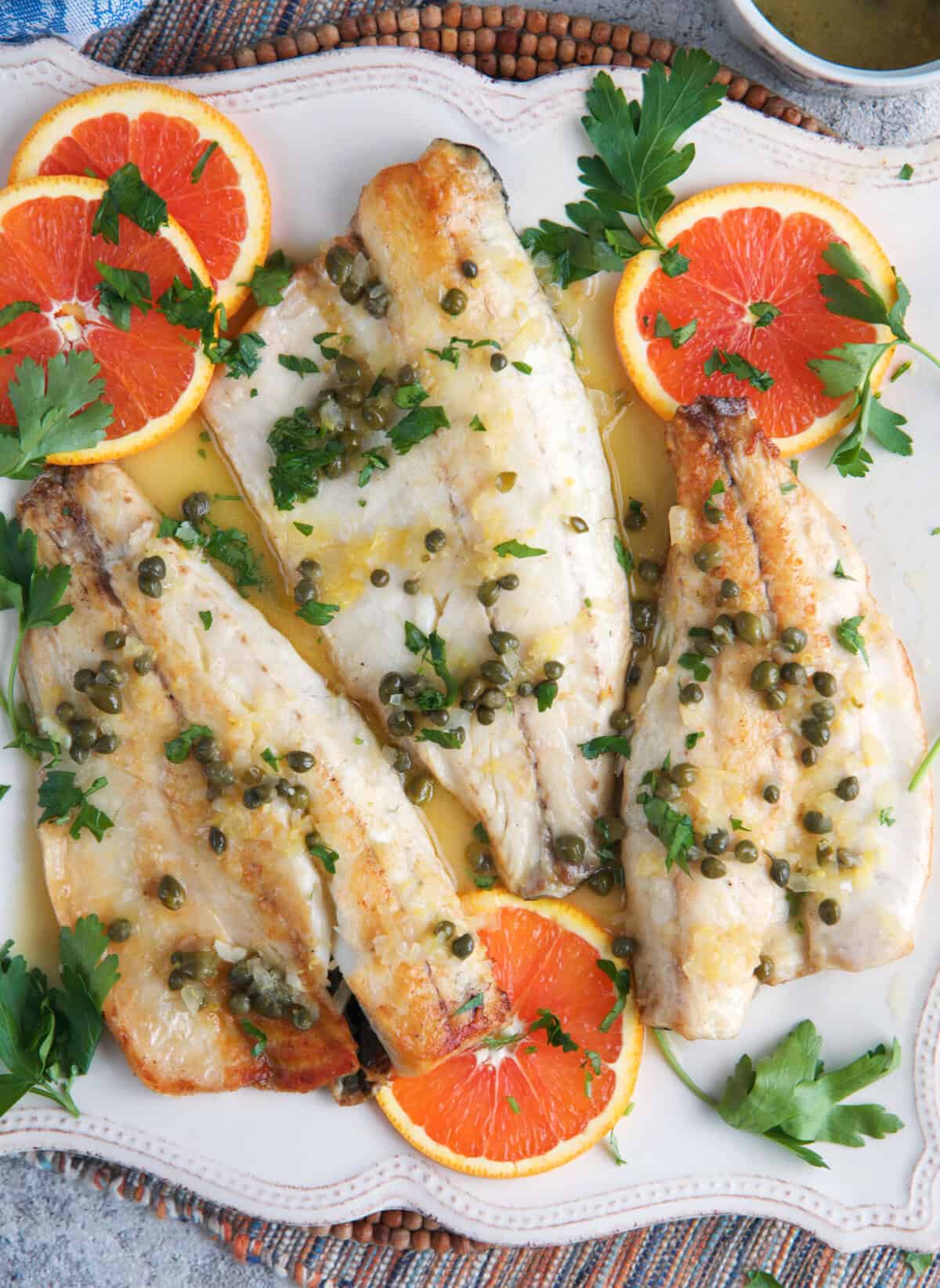 Pan Seared Bronzino filets on a white platter with sliced oranges and parsley