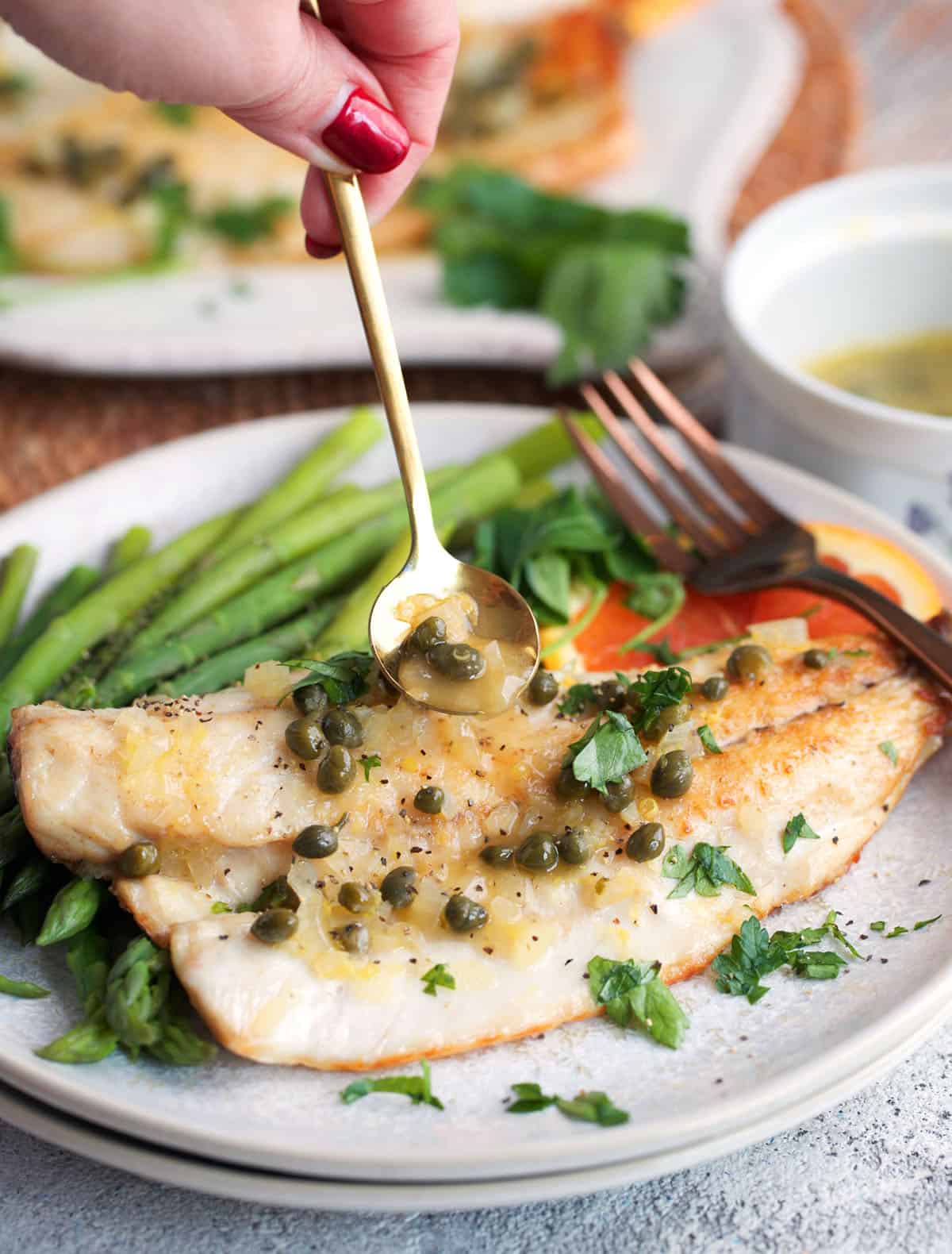 Pan Seared Banzino with sauce being drizzled over it on a plate with green beans.