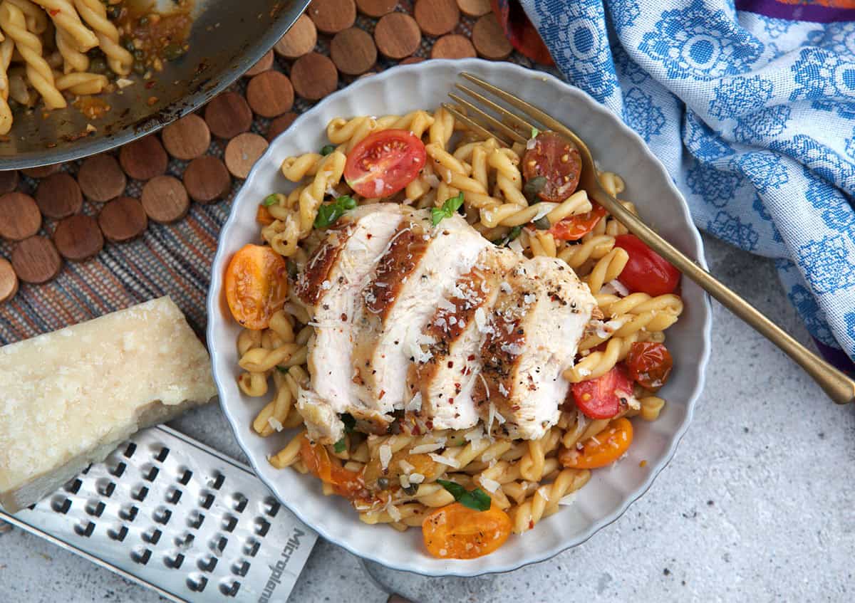 Bruschetta chicken pasta plated on a white plate with a wedge of parmesan cheese next to it for grating.