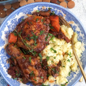 Coq au vin served in a blue and white bowl over a pile of fully mashed potatoes.