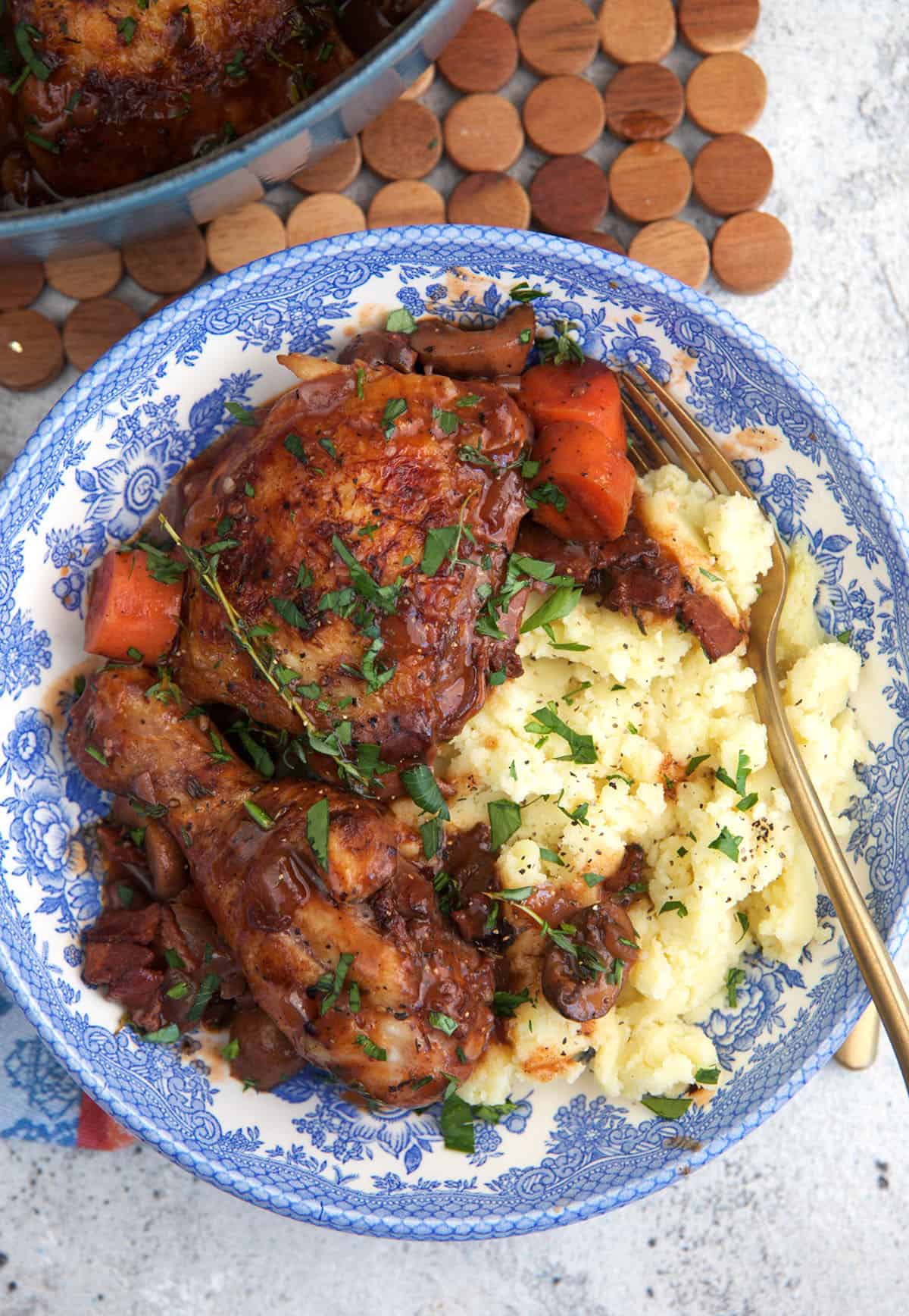 Coq au vin served in a blue and white bowl over a pile of fully mashed potatoes.
