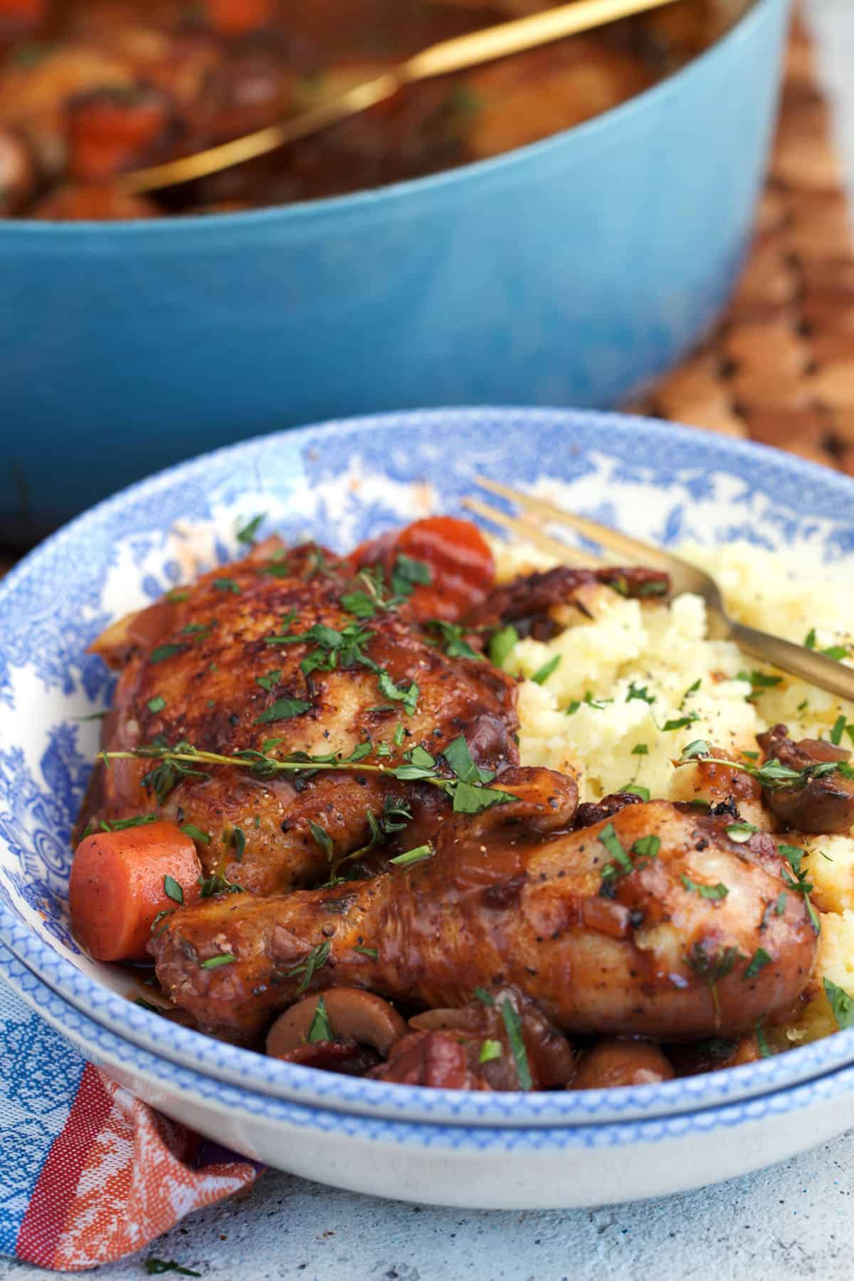 Coq au vin over mashed potatoes in a blue and white transfer ware bowl.
