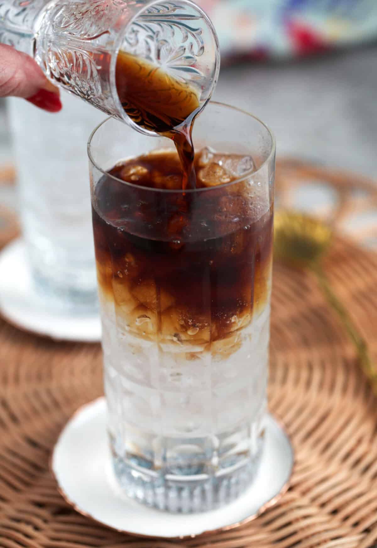 espresso being poured over tonic on ice in a tall glass