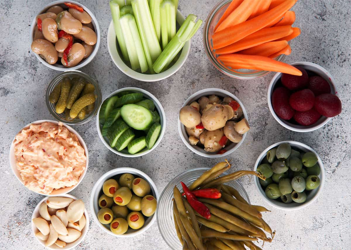 Ingredients for a relish tray show assorted vegetables, dips and olives in bowls.