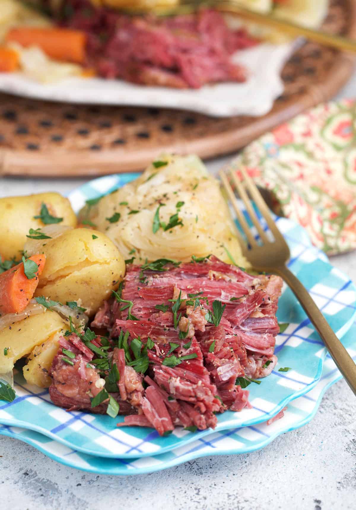 sliced corned beef on a plate with a gold fork and a side of cabbage, carrots and baby potatoes.