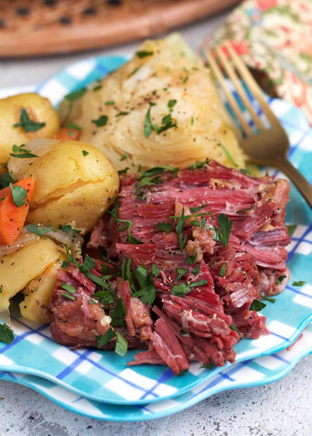 Instant Pot corned beef on a blue plaid plate with cabbage carrots and potatoes.