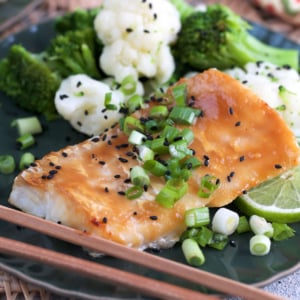 miso cod on a plate with broccoli and cauliflower topped with chopped scallions and sesame seeds.