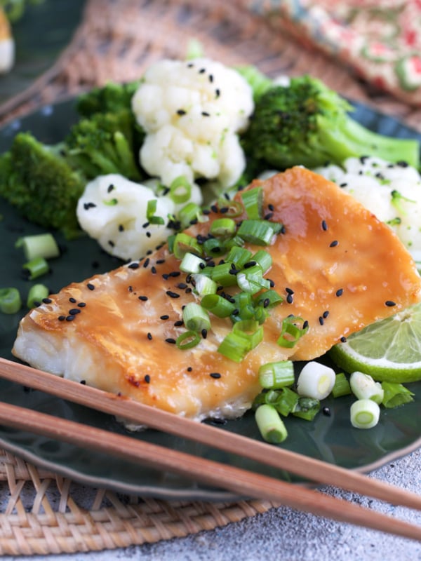 miso cod on a plate with broccoli and cauliflower topped with chopped scallions and sesame seeds.