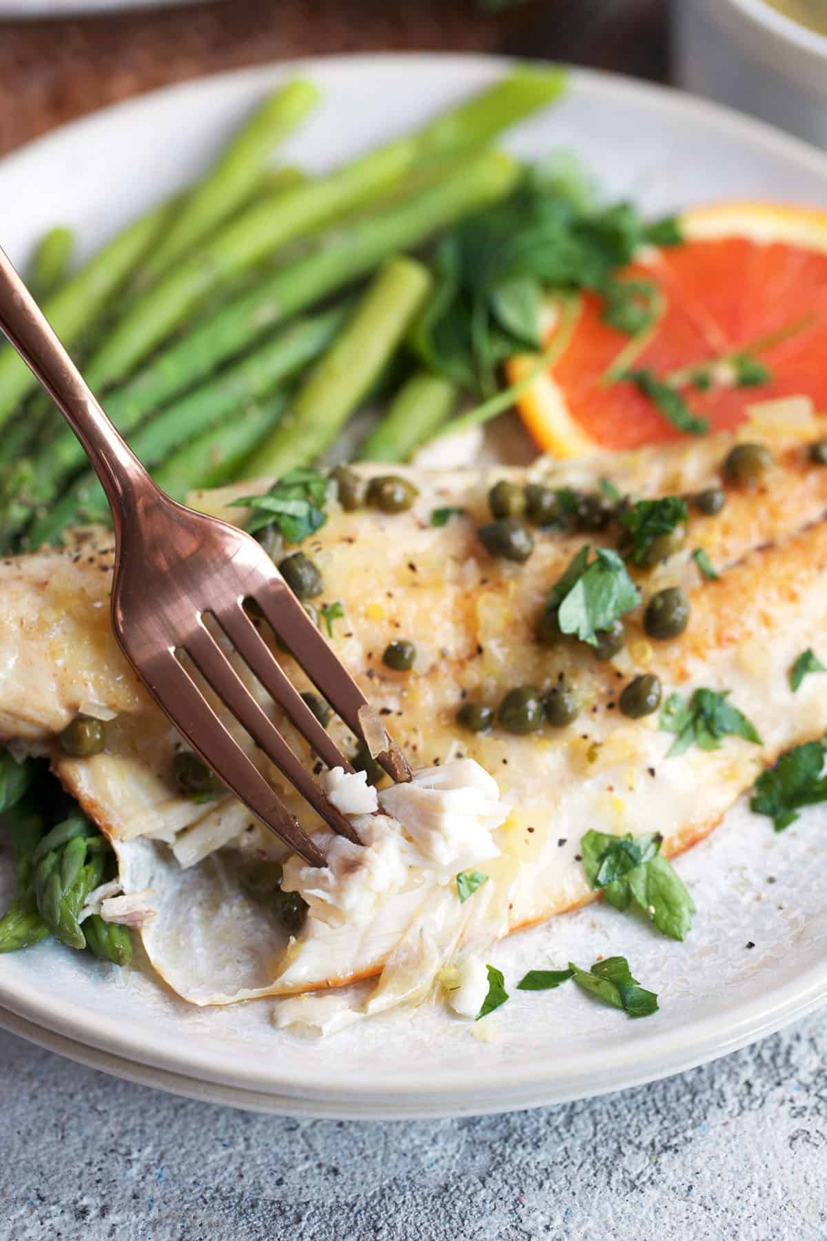 A fork flaking a piece of branzino on a plate