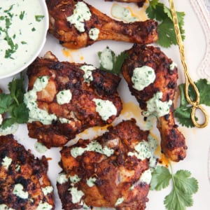 Peruvian chicken with green sauce on a white platter with cilantro and a gold serving spoon