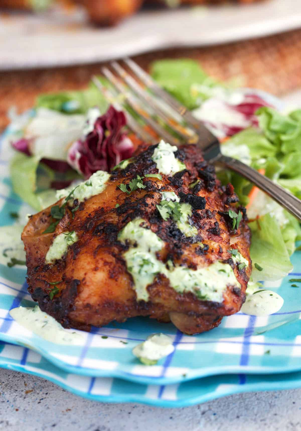 Peruvian chicken on a plaid plate, served with a salad topped with creamy green sauce.