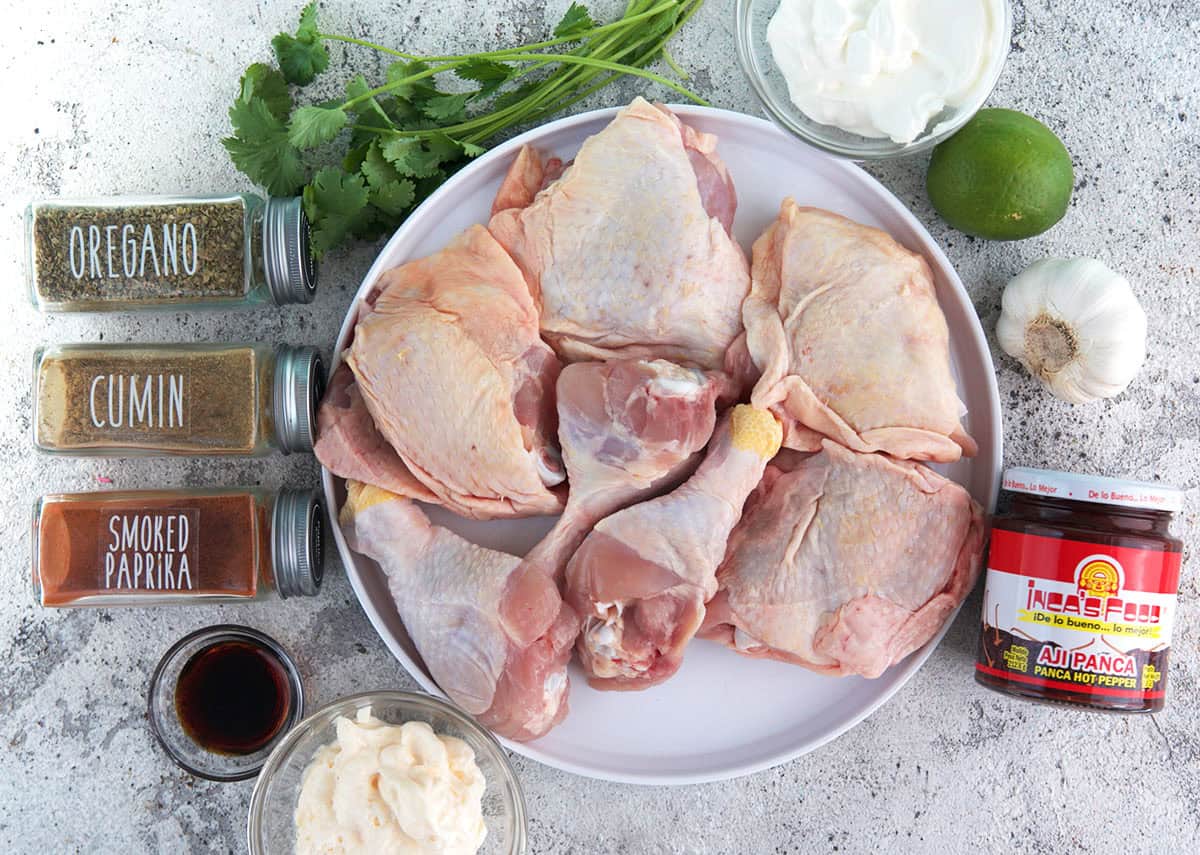 Ingredients for Peruvian chicken on a gray background, bone-in chicken, spices, greek yogurt, herbs, lime and garlic.