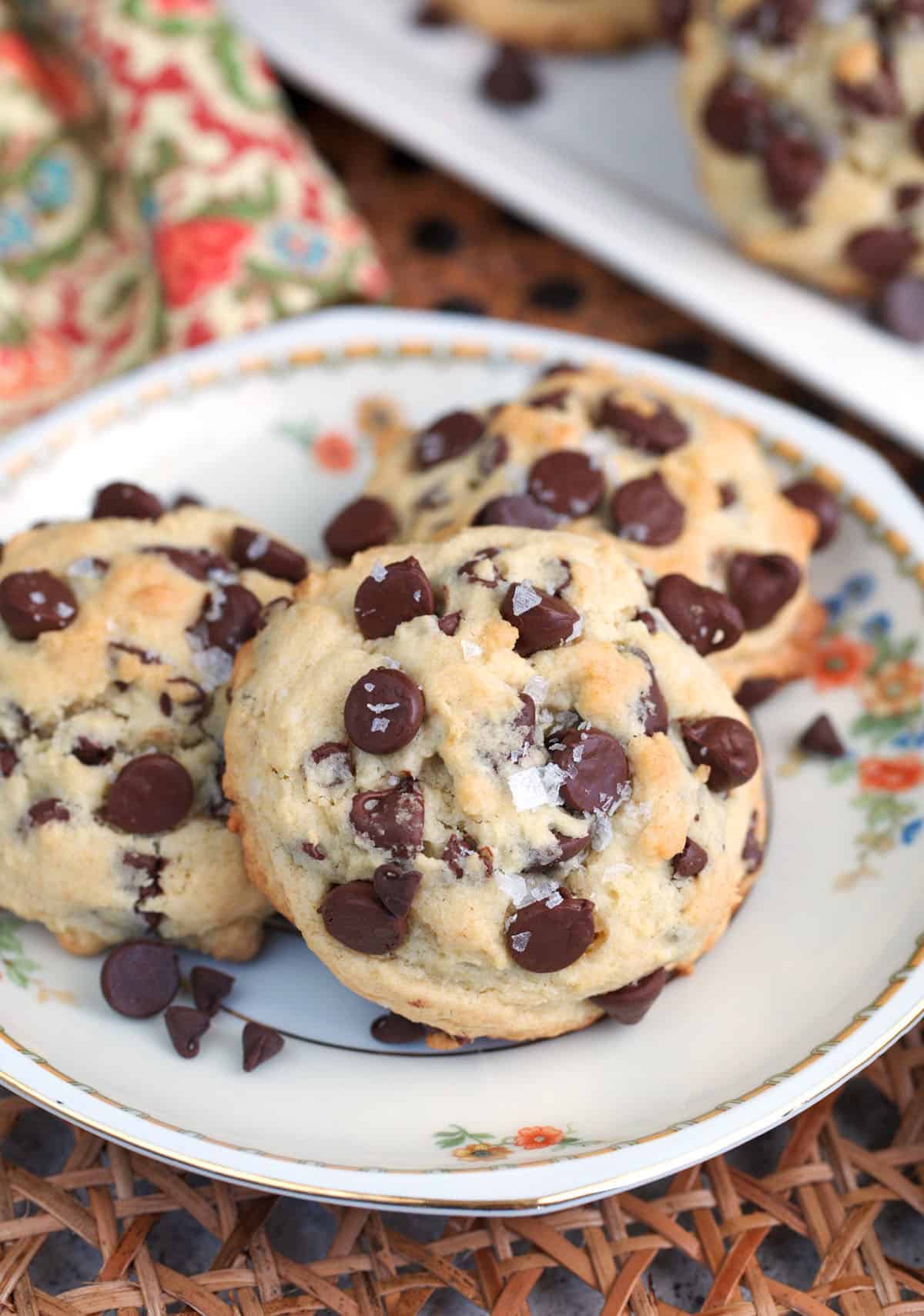 Sourdough Chocolate Chip cookies on a white plate with flowers and sprinkled with sea salt.