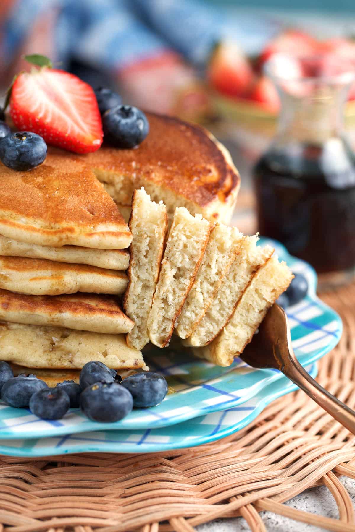Sourdough pancakes stacked on a plate and topped with berries with a bite of pancake on a fork.